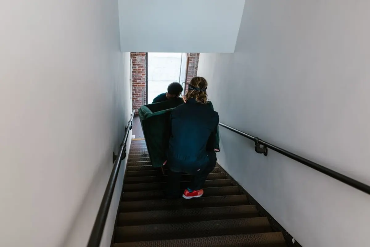 Zwei Helfer tragen ein Sofa das Treppenhaus hinauf